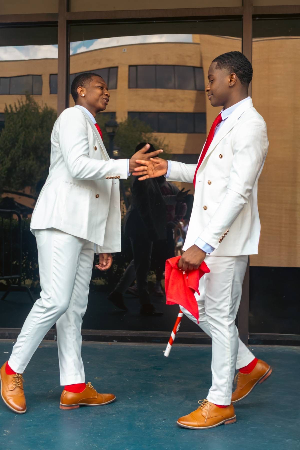 Two brothers in white suits greeting each other with a handshake