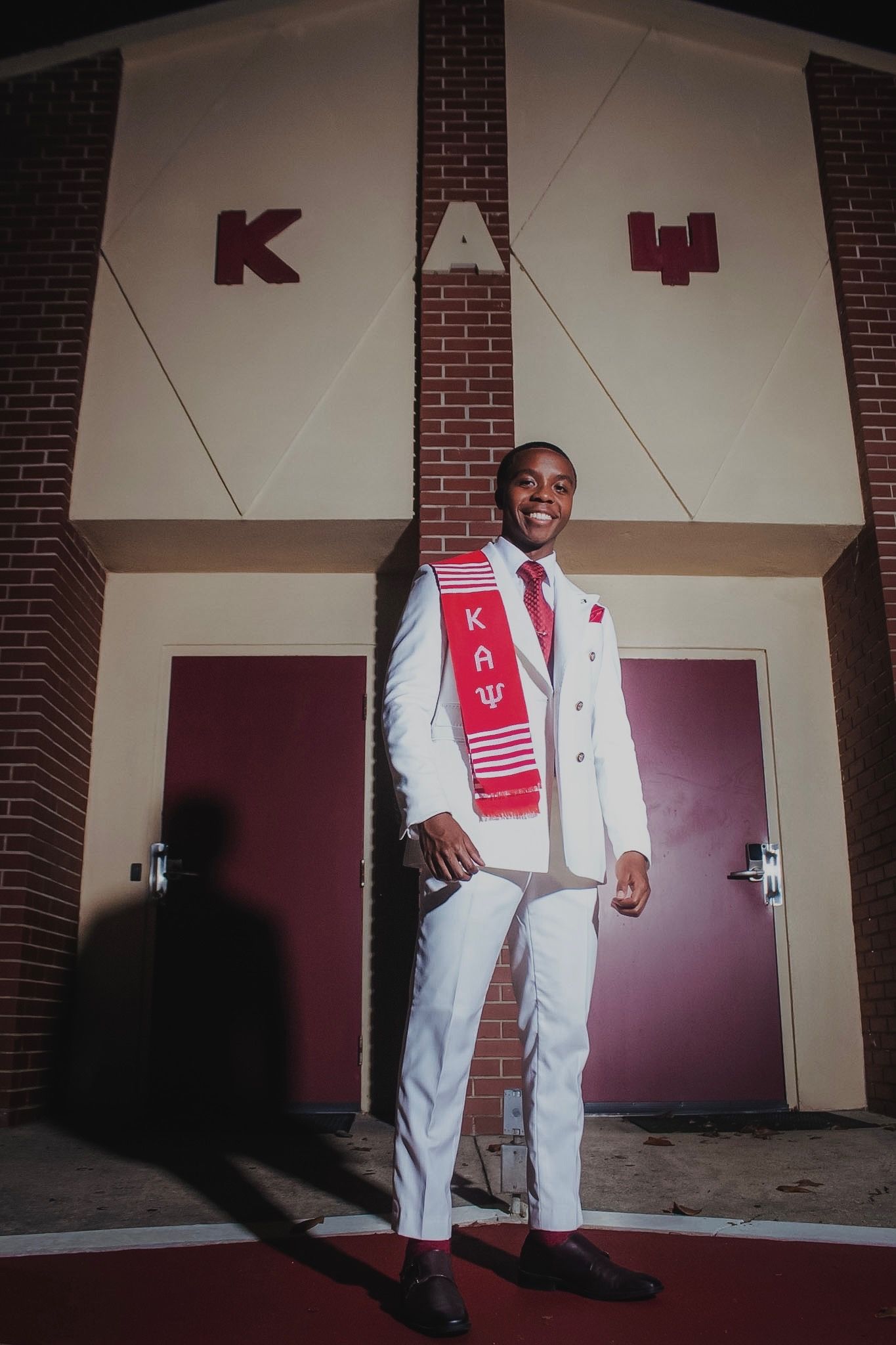A brother in a white suit and crimson kente stole outside the chapter house