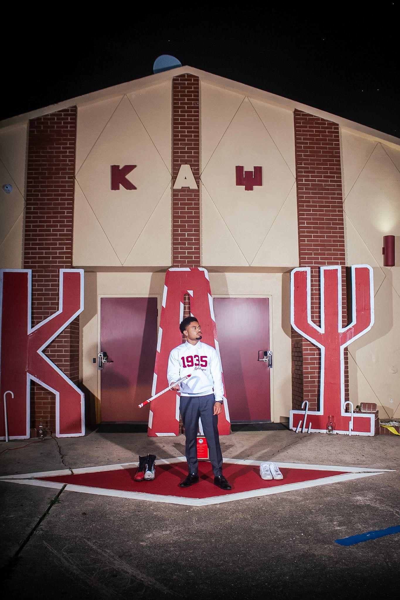 A brother holding a crimson and white cane in front of the chapter house letters at night