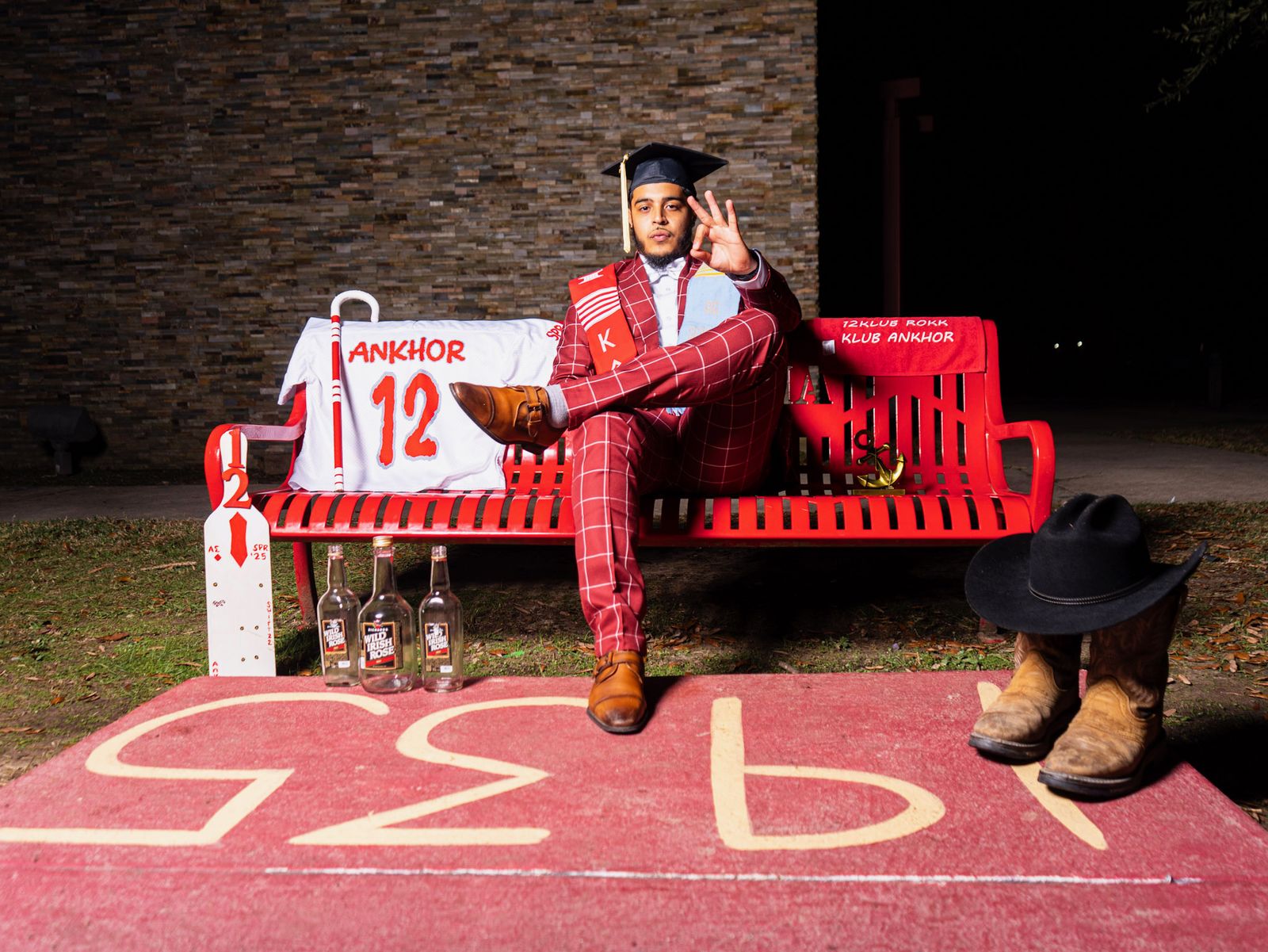 A brother in a graduation cap and crimson suit seated on a crimson bench